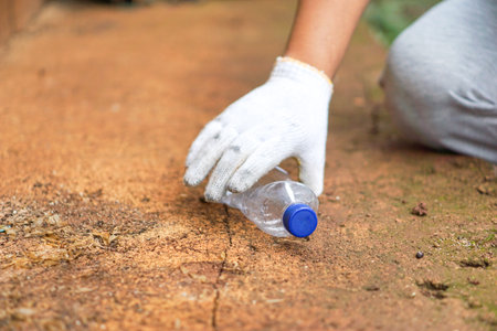 the hand of a man wearing white gloves picking up plastic bottle waste