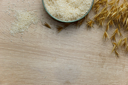 A pile of uncooked white rice in a bowl on a wooden tableの写真素材
