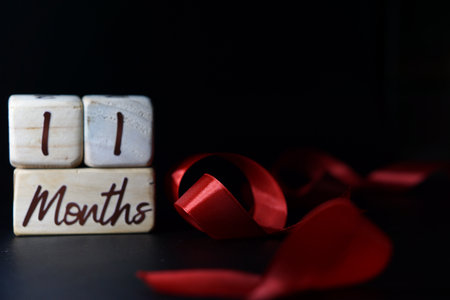 Baby's age milestone written on a wooden cube with a red ribbon on a black background