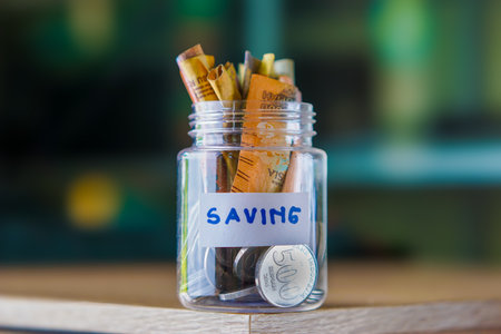 Coin and banknote savings in a clear glass bottle with bokeh background. finance and accounting savings investment conceptの写真素材