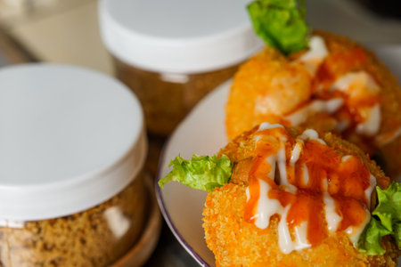 close-up photo Fried patties filled with lettuce and sausage topped with hot sauce and mayonnaise, served on a white plate with a jar on the side. selective focusの写真素材