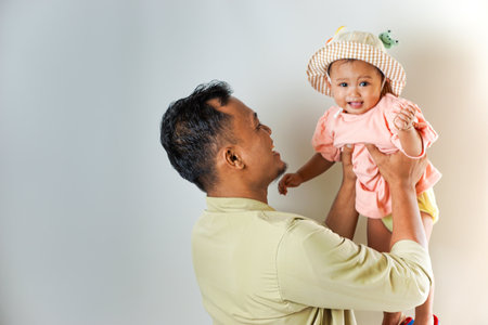 A happy father holding his adorable baby daughter in a cute hat. They are both smiling warmly,...