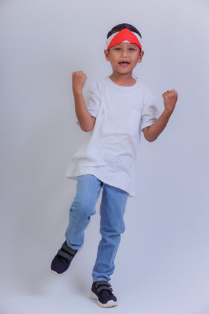 A young boy in a white t-shirt and jeans cheerfully poses with a red and white headband.の写真素材