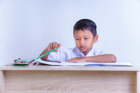 A Indonesian young boy in a school uniform is studying at a desk with pencils and books.の写真素材