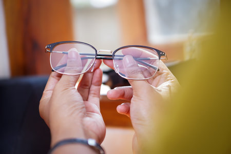 A close-up of hands delicately holding a pair of glasses, showcasing craftsmanship and attention to detail.の写真素材