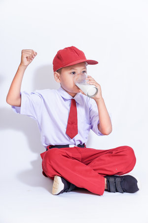 A cheerful child in a red cap and uniform outfit enjoys a glass of milk, celebrating good health and happiness.の写真素材
