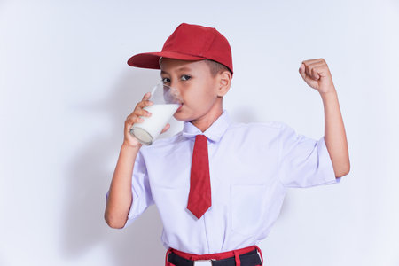 A confident boy in a red cap enjoys a glass of milk, promoting strength and health with a triumphant pose.の写真素材