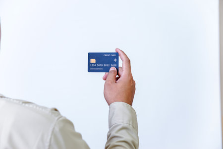 A hand holding a modern credit card with a microchip against a plain background.