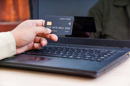 A person holds a credit card in front of a laptop, indicating online transactions.
