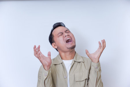 A man expresses frustration with his hands on his head and a shout.の写真素材