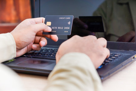 A person holds a credit card in front of a laptop, indicating online transactions.の写真素材