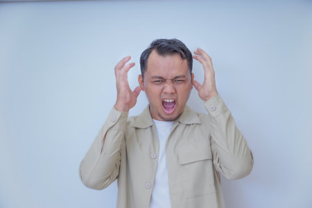 A man expresses frustration with his hands on his head and a shout.の写真素材