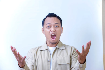 A surprised man expressing excitement and shock with wide open mouth and raised hands.