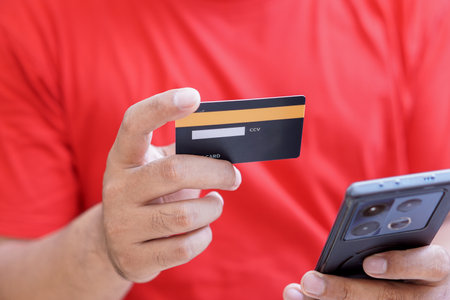 A person with red t-shirt holding a credit card in one hand and a smartphoneの写真素材