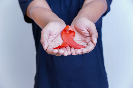 A person holding a red ribbon, symbolizing awareness and support for health issues.