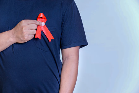 a man holds a red ribbon and tapes it to his chest, symbolizing awareness and support for important causesの写真素材