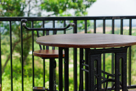 A wooden table and chair set on a balcony with a lush green view.の写真素材