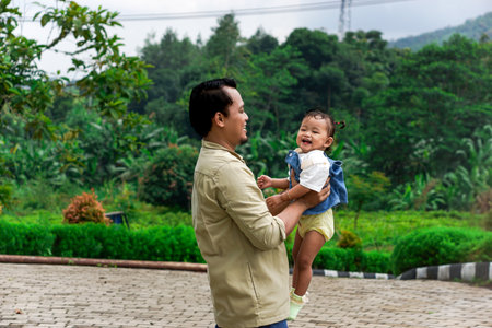 A joyful moment between a Asian father and his smiling daughter in a beautiful green park. concept of fater's dayの写真素材