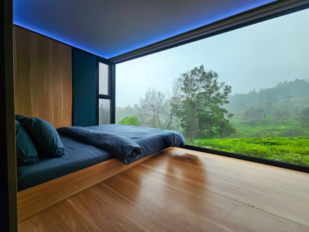 Modern bedroom with large window overlooking misty green landscape.の写真素材