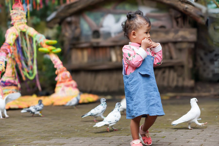 A young asian girl playing joyfully among pigeons in a vibrant outdoor setting.の写真素材