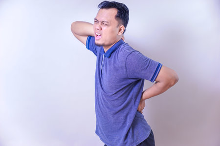 An asian man is experiencing discomfort, holding his shoulder and showing signs of pain.