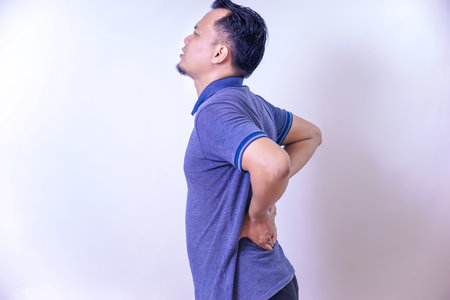 An Asian man experienced discomfort, holding his waist and showing signs of pain.