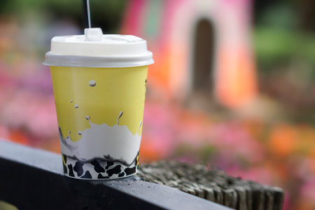 A vibrant yellow cup sits on a wooden fence, surrounded by colorful floral scenery.