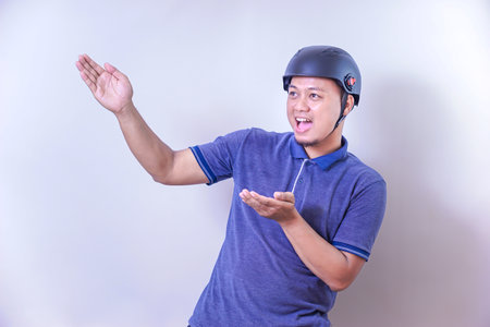 Excited asian man with helmet gestures enthusiastically to present somethingの写真素材