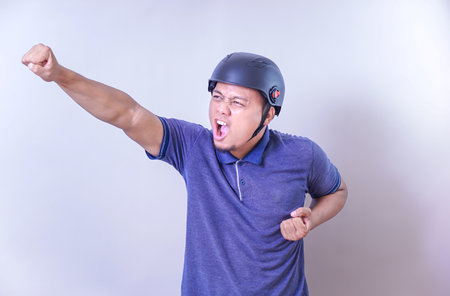 An asian man wearing a helmet passionately expresses excitement with a raised fist.