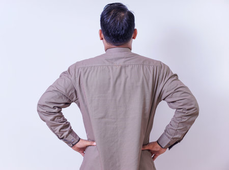 back view of An asian man in a brown shirt stands with hands on hips
