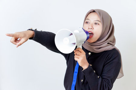 A woman passionately speaks through a megaphone while pointing forward.の写真素材
