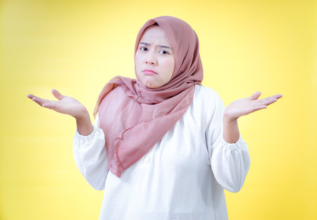 An asian woman with a hijab shows a confused expression against a yellow background.の写真素材