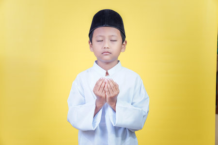 A young asian boy in prayer attire reflects the spirit of Ramadan Kareem with devotionの写真素材