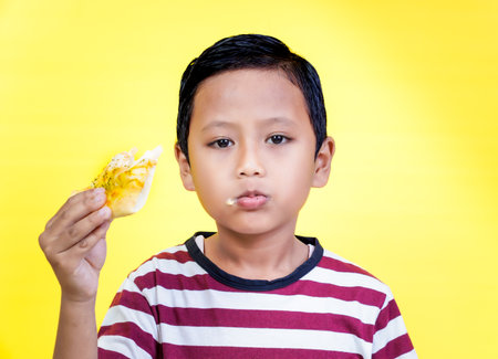 An asian young boy enjoys a delicious slice of pizza against a bright yellow background.の写真素材