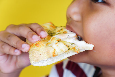 A child eagerly bites into a cheesy slice of pizza, enjoying a delicious moment. international foods day conceptの写真素材