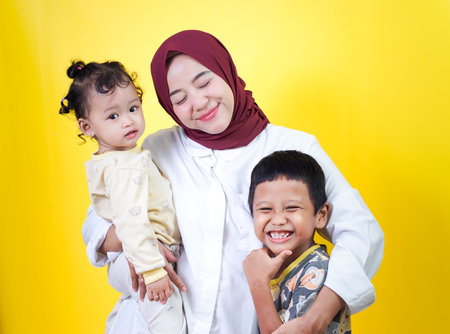 A joyful asian mother holds her two happy children against a bright yellow background. mothers day conceptの写真素材