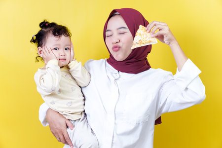 A joyful woman holds her smiling toddler and a piece of pizza against a bright yellow background, mothers day conceptの写真素材