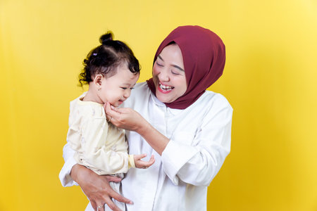 A joyful asian mother interacts with her happy child against a bright yellow background.の写真素材