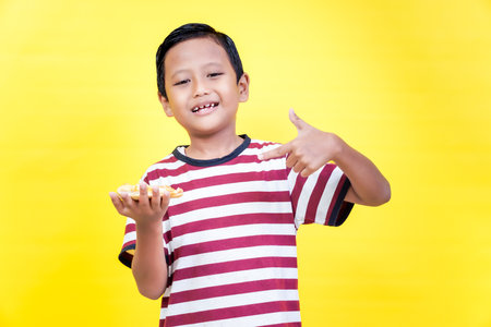 A cheerful asian boy in a striped shirt holds a slice of food and gives a thumbs up against a bright...