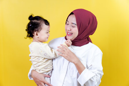 A joyful asian mother interacts with her happy child against a bright yellow backgroundの写真素材