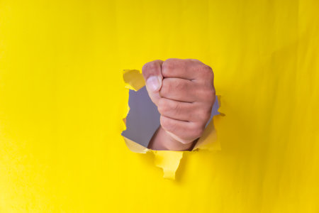 A fist breaks through bright yellow paper, symbolizing strength and determination.の写真素材