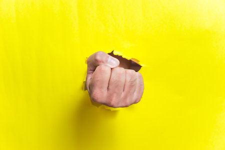 A fist breaks through bright yellow paper, symbolizing strength and determination.の写真素材