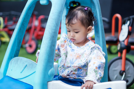 An asian toddler girl plays inside a blue toy car, exploring and enjoying her time at the...