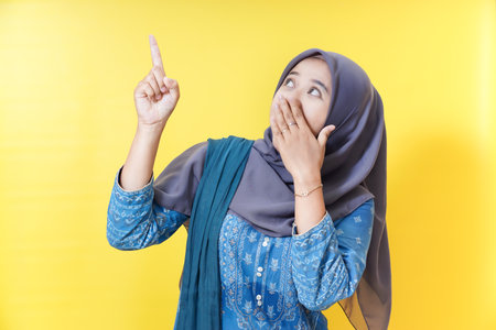 Woman in hijab pointing up, surprised.の写真素材