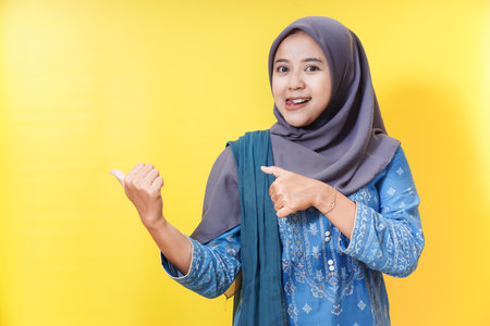 Smiling woman in hijab pointing and gesturing on yellow background.の写真素材