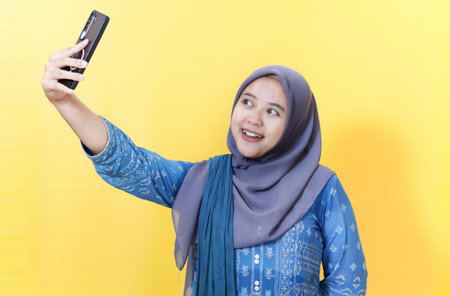Woman in hijab taking selfie against yellow background.の写真素材