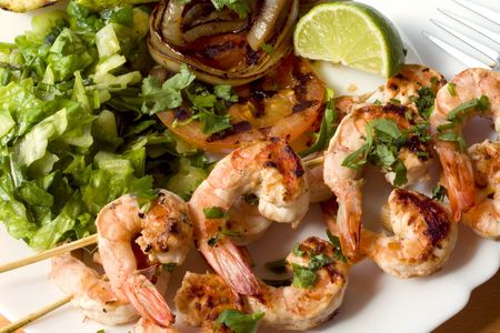 Grilled prawns on bamboo sticks served with salad and grilled vegetables in dinner setting. の写真素材