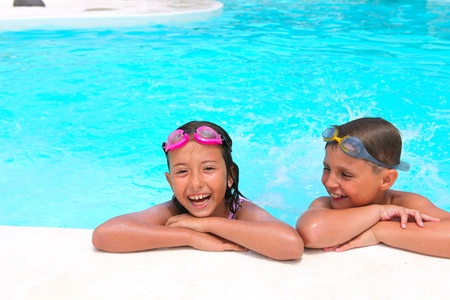 Happy children,  girl and boy, relaxing on the side of a swimming pool wearing pink and grey goggles