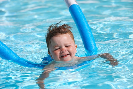 Happy little boy learning to swim with pool noodleの写真素材
