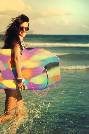 Happy girl running laughing cheerful having fun with bodyboarding surfboard on summer holidays の写真素材